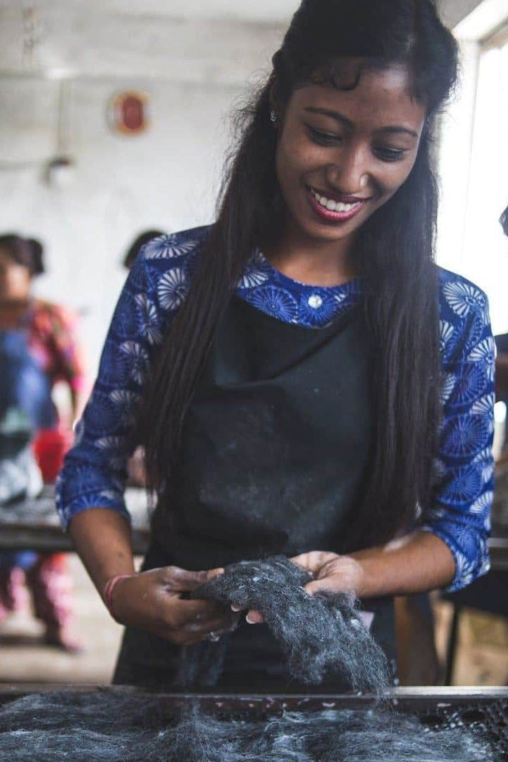 En smilende kvinde arbejder med rå uld i produktionen af SHUS.dk håndlavede uldtøfler i et værksted i Nepal